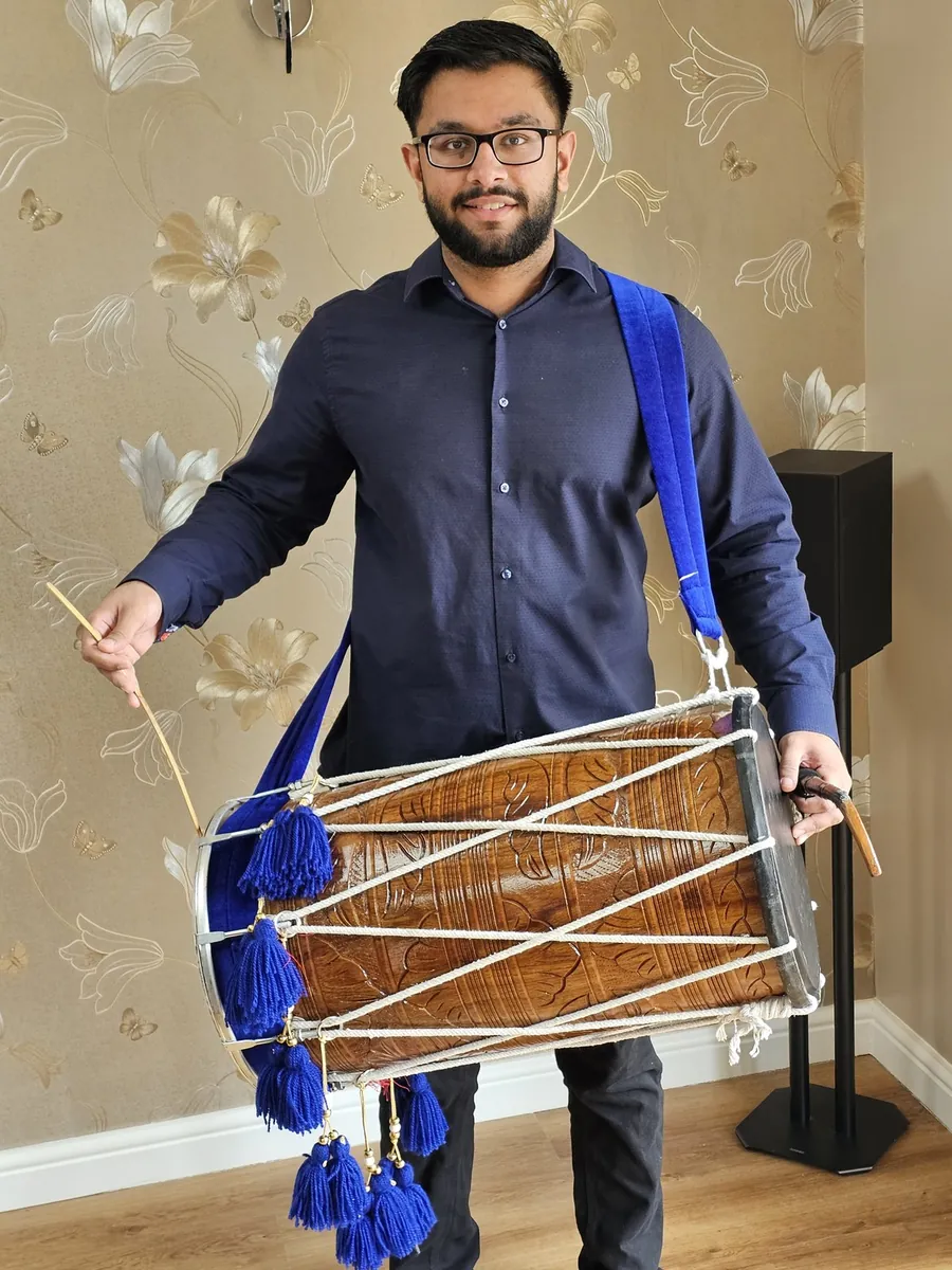 Manraj smiling with his carved wooden dhol on a blue strap