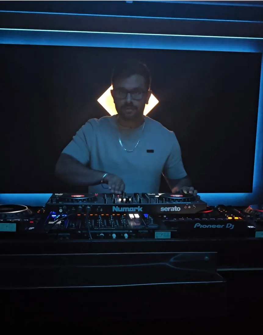DJ Manraj at the decks, lit by a diamond of light behind him